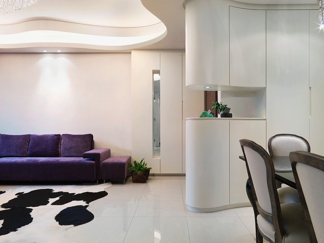 Open living room with futuristic ceiling design and dining area in front of a cupboard serving as a room divider