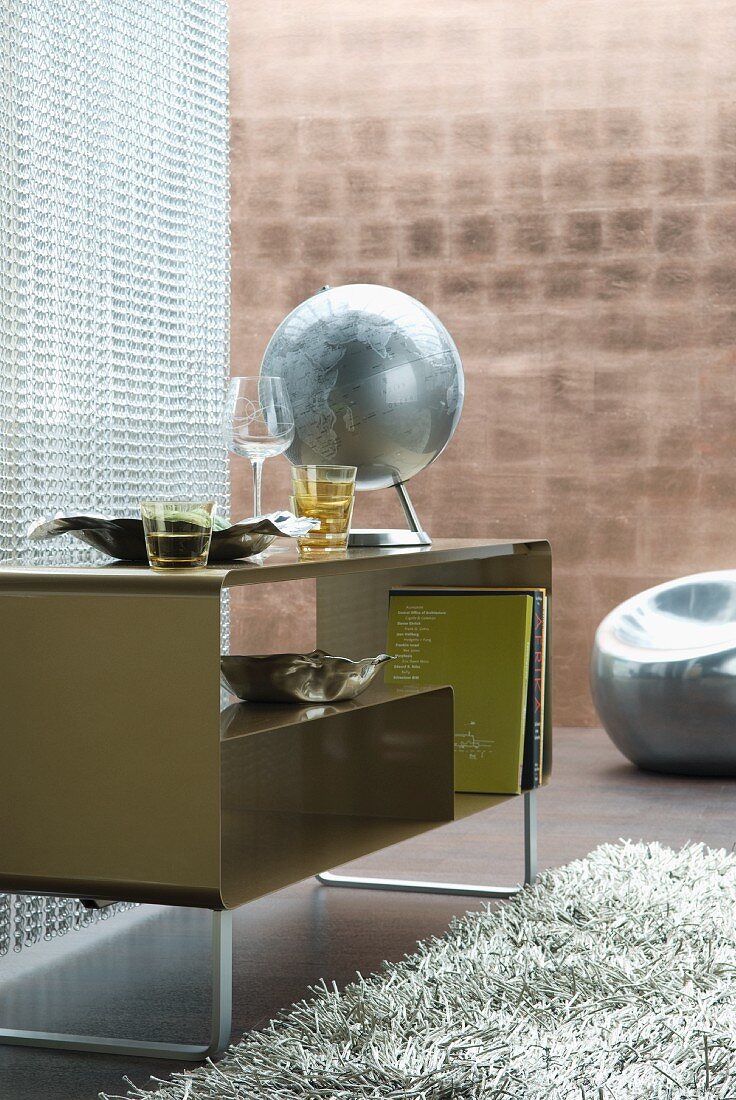 Globe on retro cabinet in front of plastic partition and copper-coloured wall in background