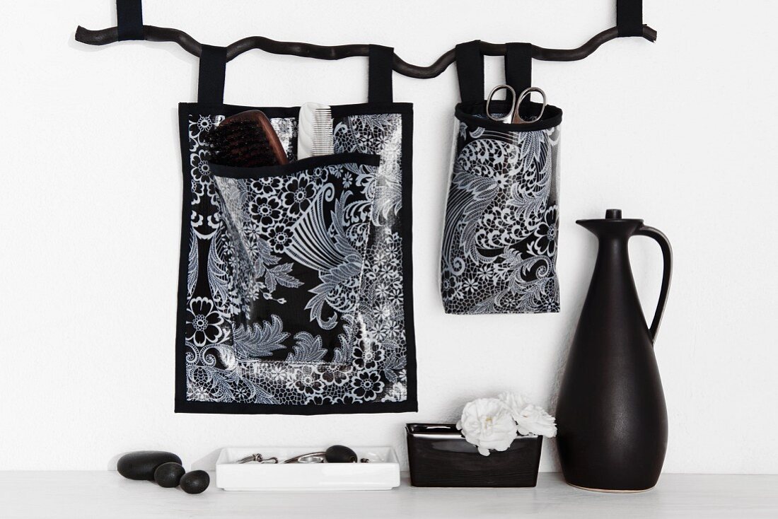 Black and white patterned storage bags hung on wall and black jug on white surface