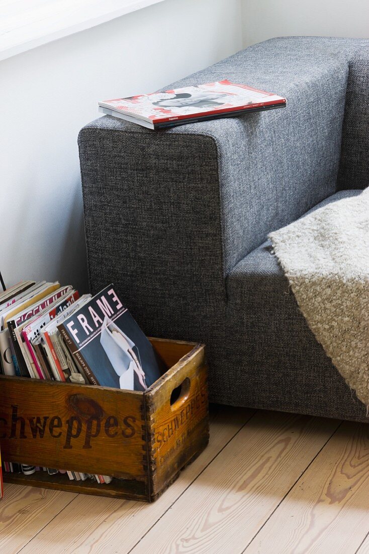 Vintage Holzkiste mit Büchern neben teilweise sichtbarer moderner Couch mit grau meliertem Stoffbezug