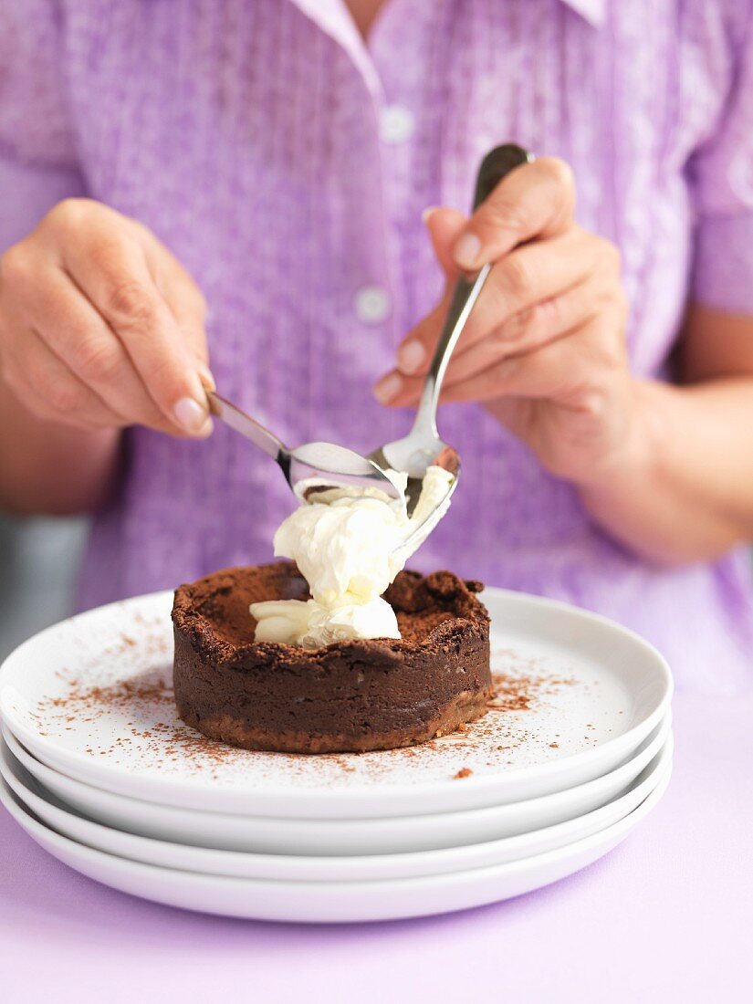 A woman adding cream to a mini chocolate cake