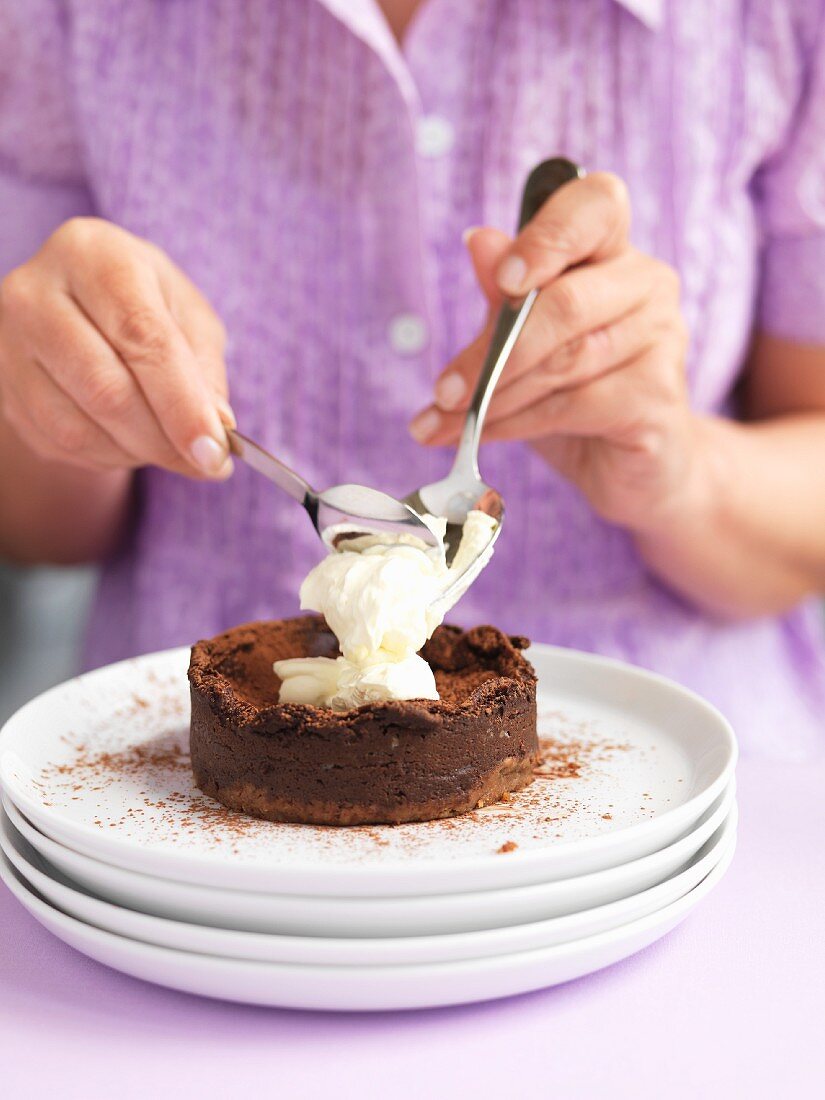 Frau gibt Sahne auf kleinen Schokoladenkuchen