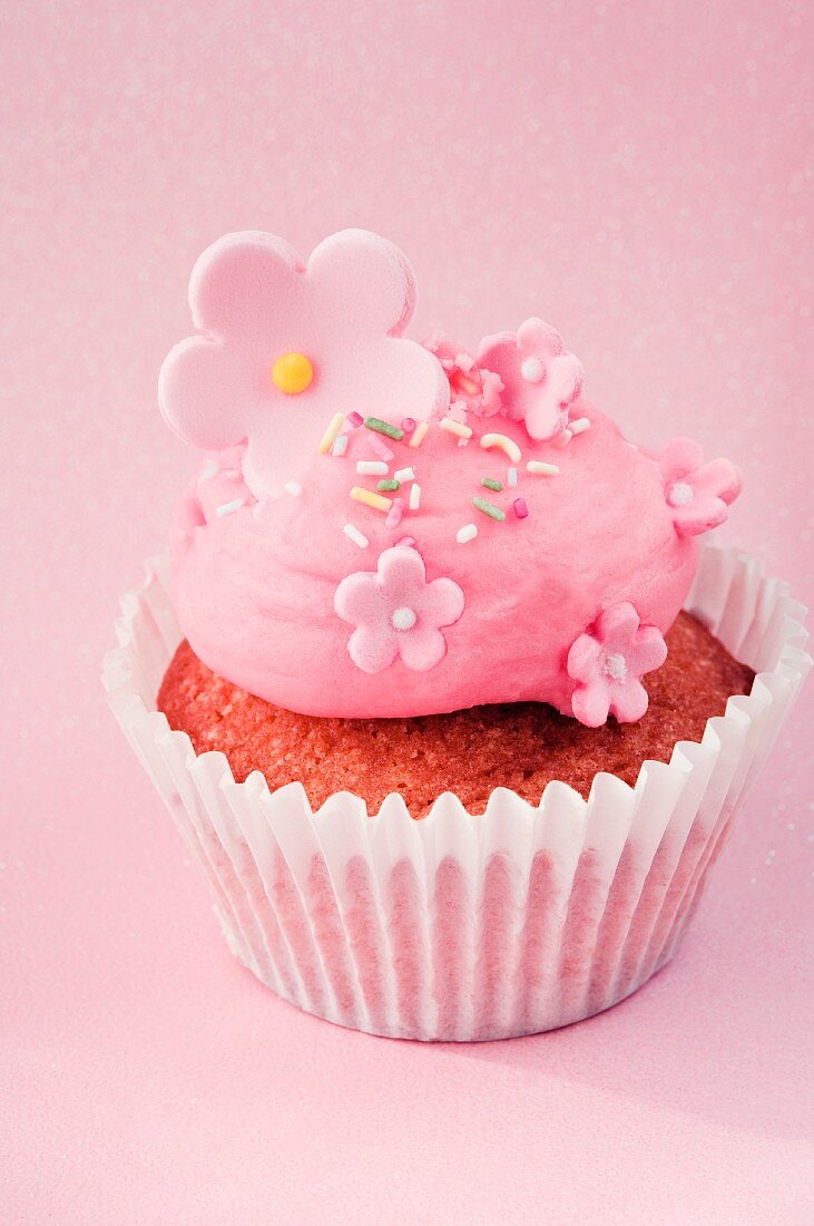 A cupcake decorated with pink cream and sugar flowers