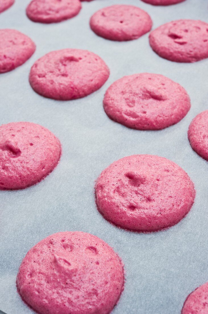 Pinkfarbene Teighäufchen für Macarons auf Pergamentpapier