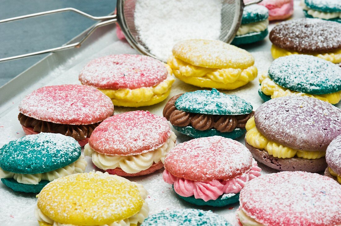 Various macaroons dusted with icing sugar on a baking tray