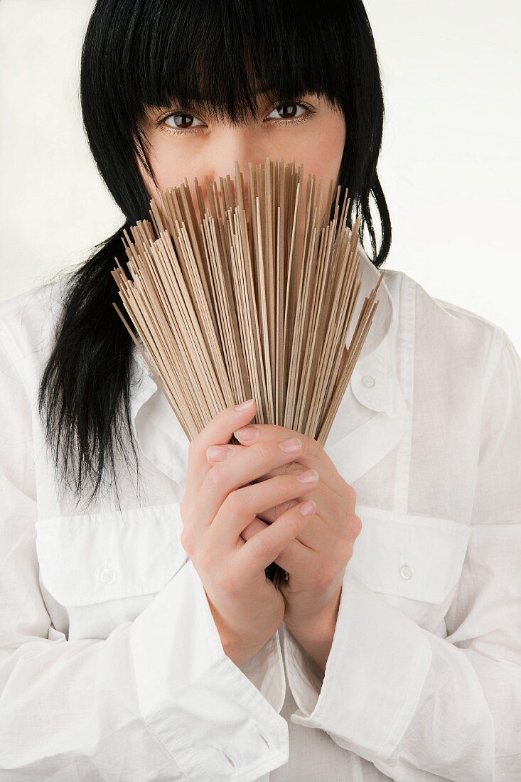 An Oriental woman in a white shirt holding Japanese soba noodles in front of her face
