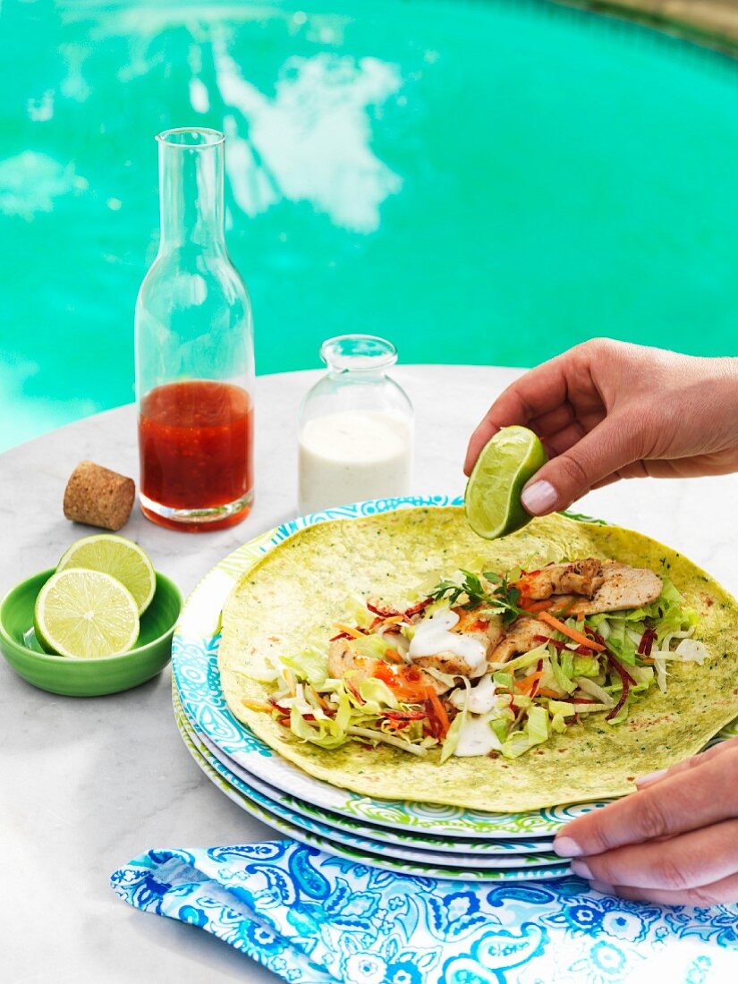 A chicken wrap being drizzled with lime juicce