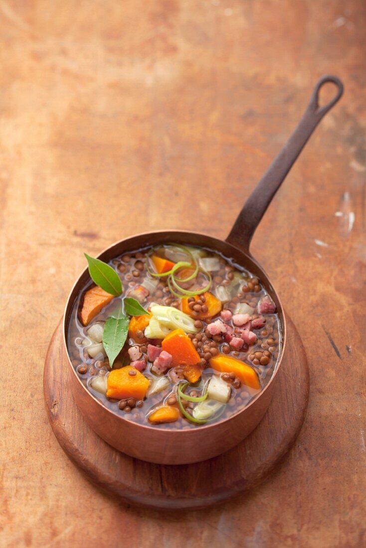 Lentil soup with diced bacon in a copper pan