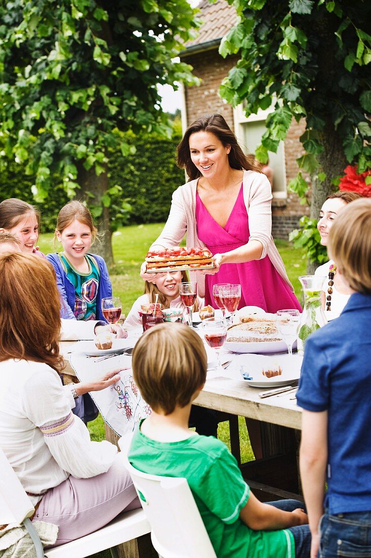 Frau bietet stellt Erdbeerkuchen bei einer Gartenparty auf den Tisch