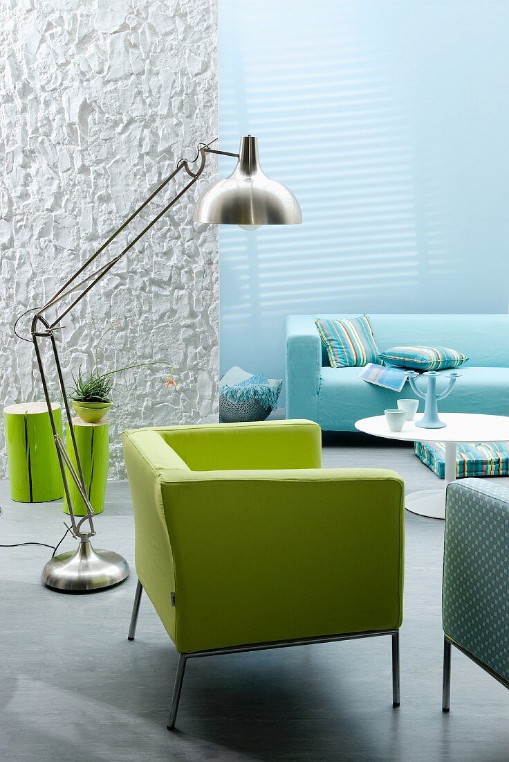 Wohnraum in Aquafarben mit grünem Sessel & Designer-Edelstahlleuchte, im Hintergrund blaues Sofa