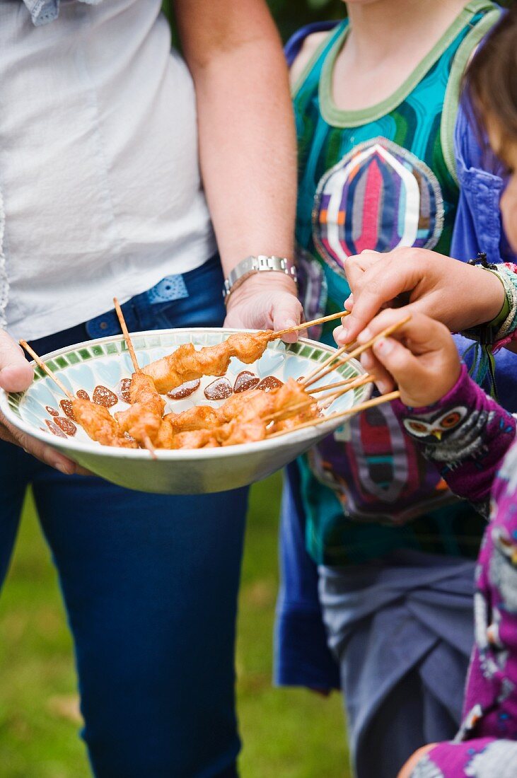 Hands reaching for chicken skewers