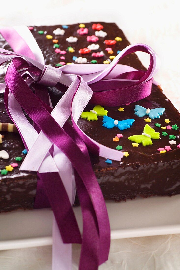 Schokoladenkuchen mit Zuckerblüten, Schmetterlingen und Geschenkband
