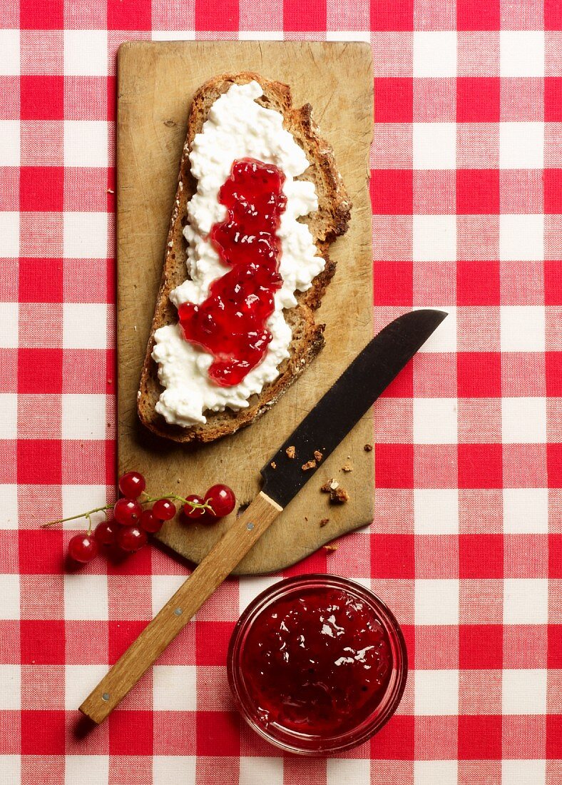A rustic slice of bread topped with cream cheese and redcurrant jam