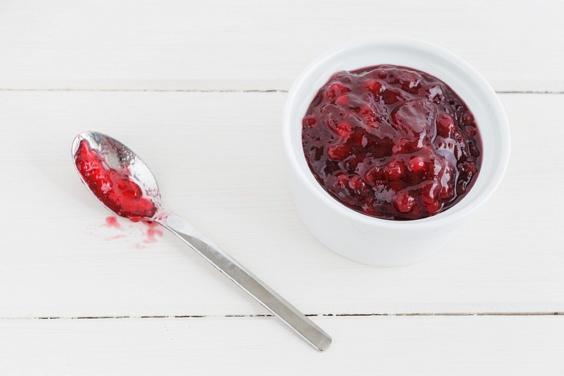 Stewed lingonberries in a bowl with a spoon