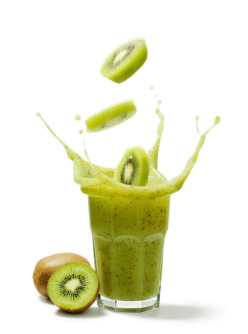 Kiwi slices falling into a glass of kiwi juice