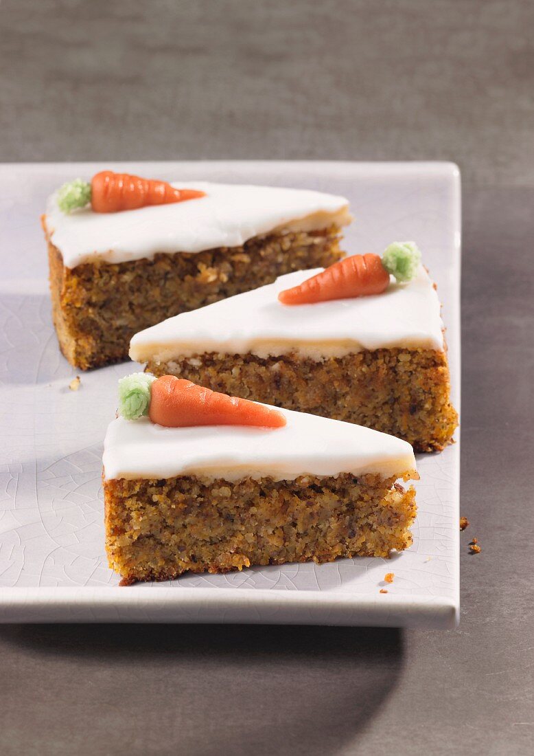 Three slices of carrot cake topped with icing and marzipan carrots