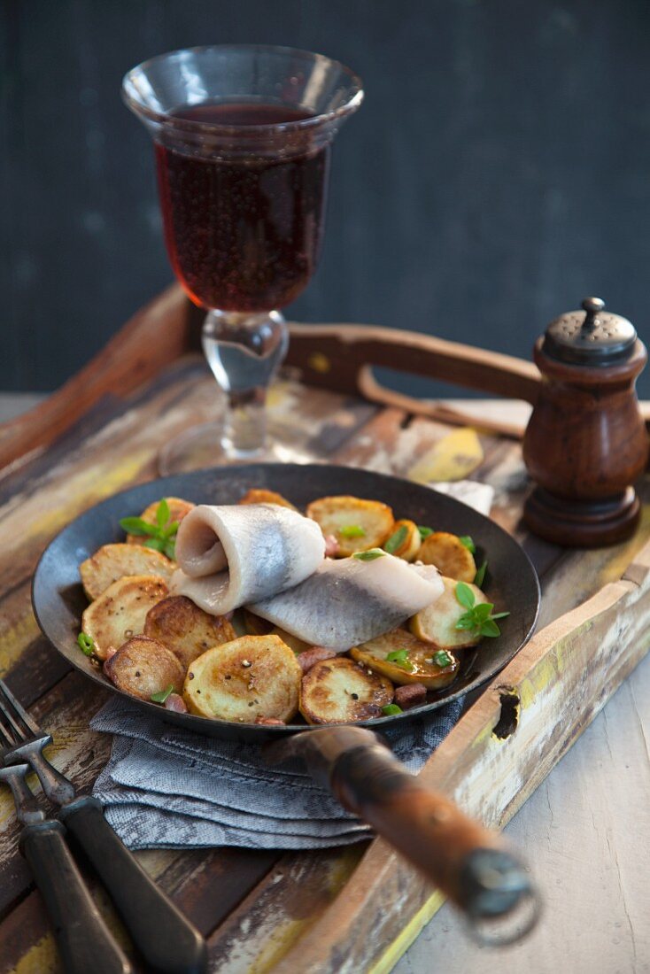 Matjes mit Bratkartoffeln in der Pfanne, dazu ein Glas Rotwein