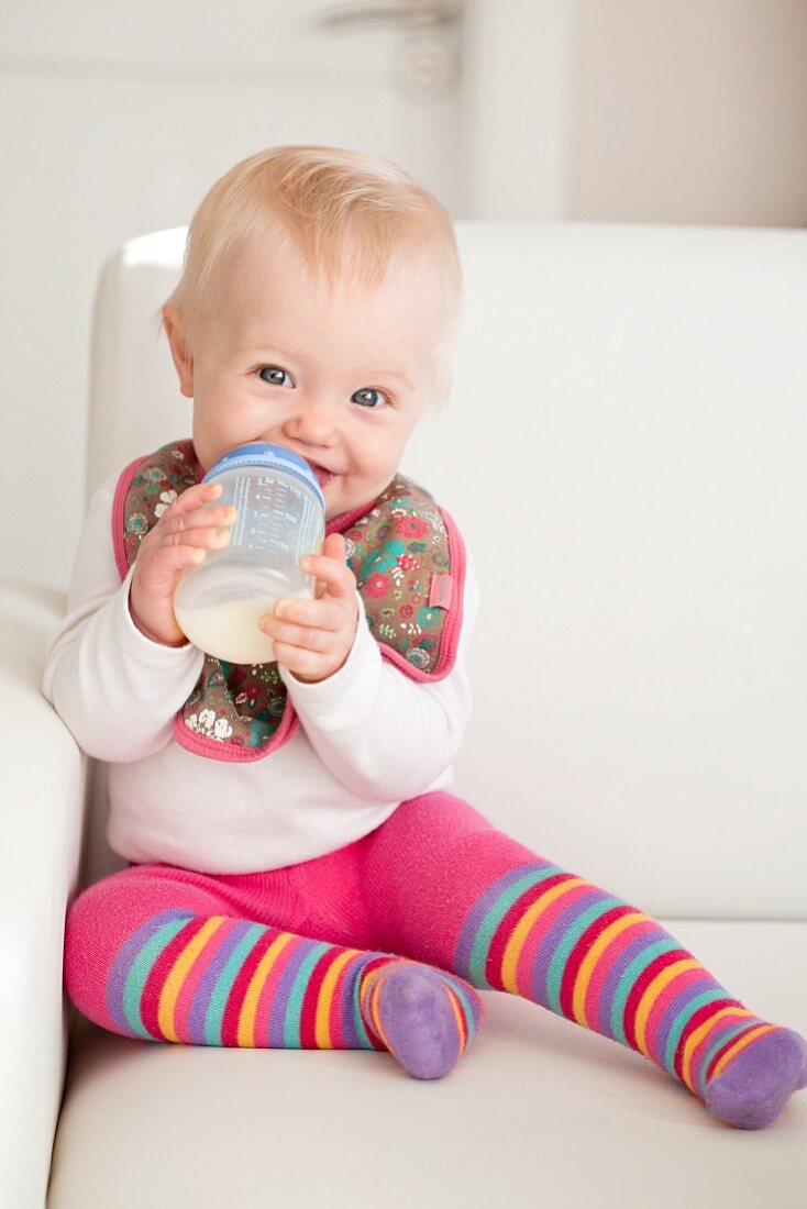 Baby mit Milchflasche auf Sofa sitzend