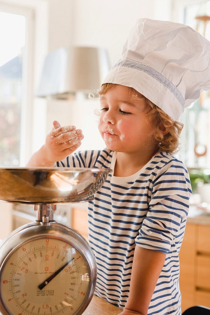 Kleiner Junge mit Kochmütze spielt mit Mehl