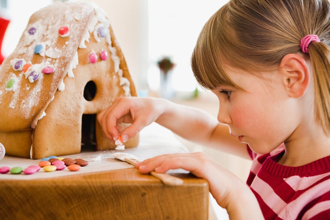 Kleines Mädchen beim Verzieren eines Lebkuchenhauses