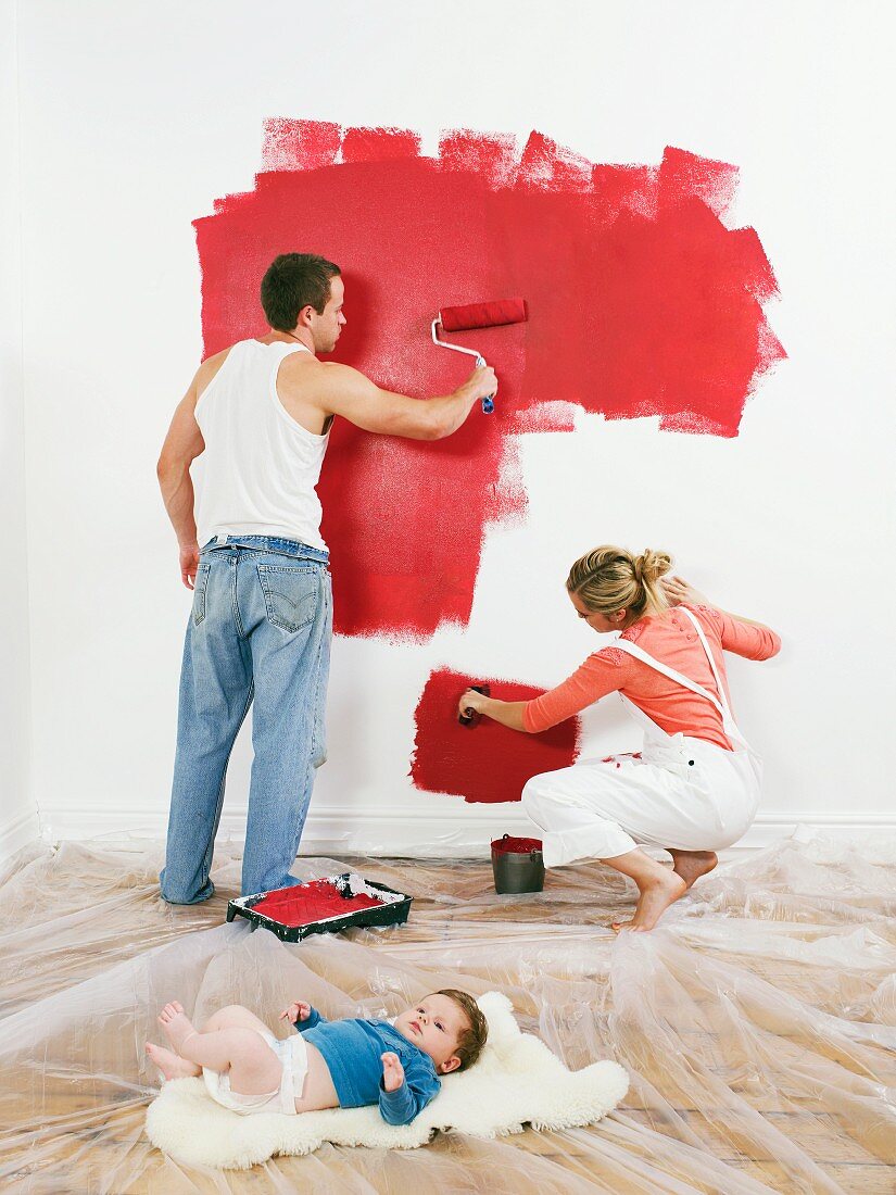 Couple painting a wall, baby on floor