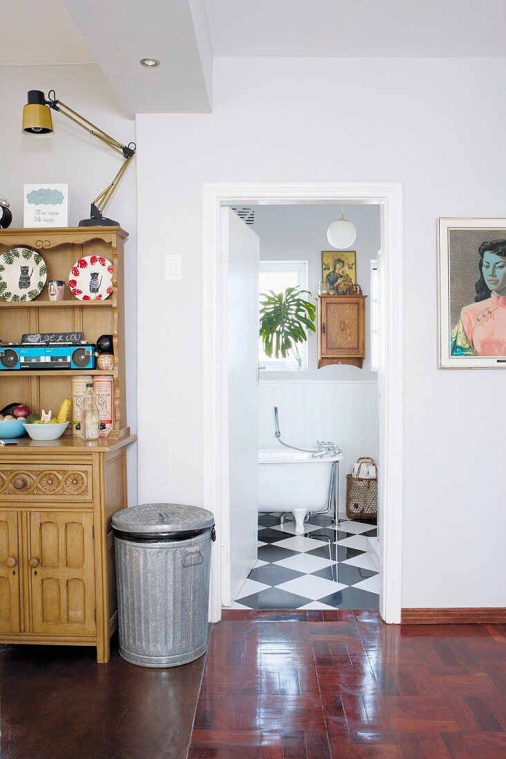 Metal dustbin next to dresser in hallway and view though open door into bathroom with black and white chequered floor