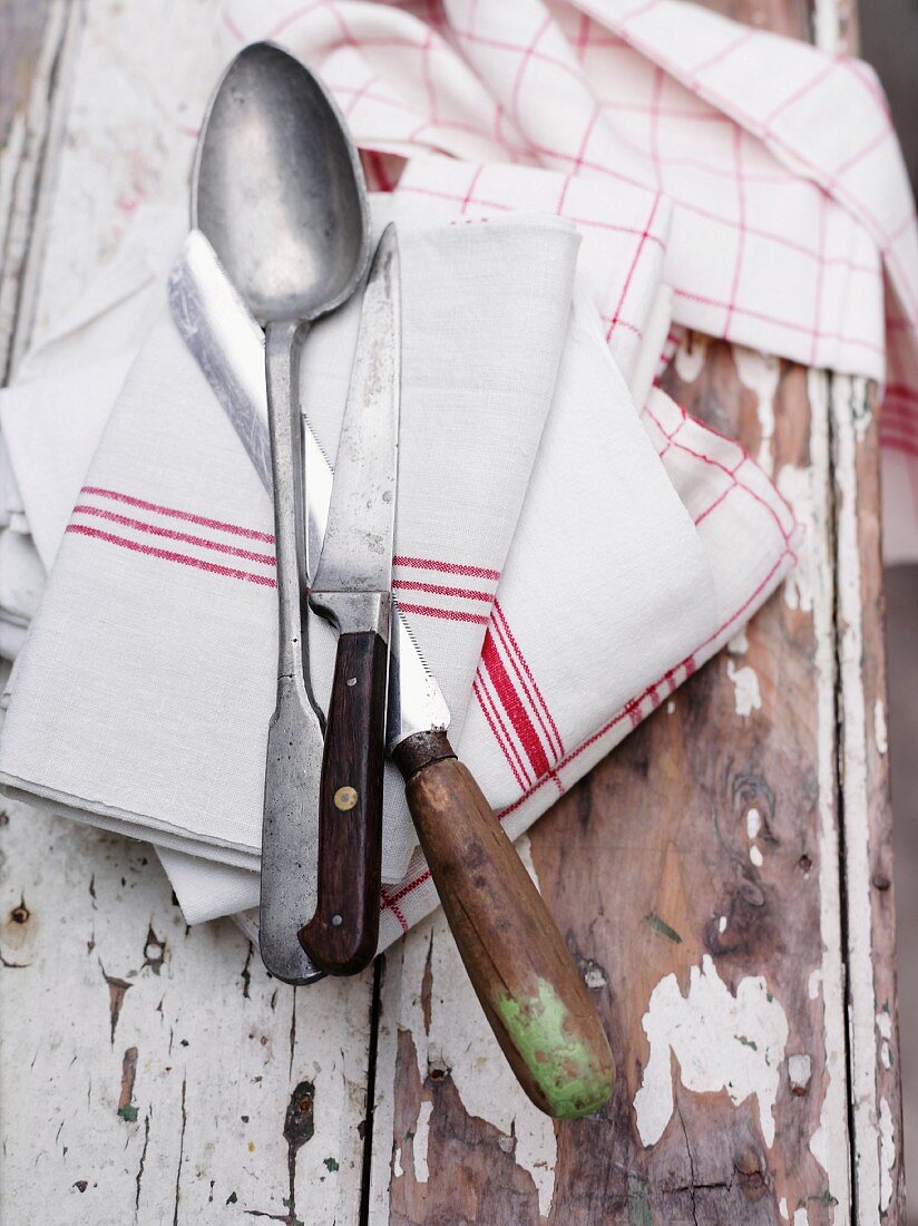 Löffel, zwei Messer & Geschirrhandtücher auf Holzuntergrund