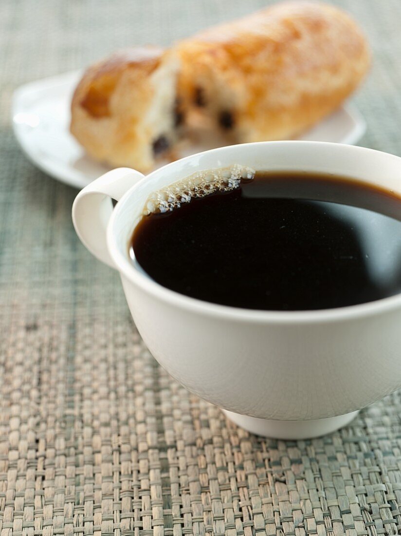 Eine Tasse schwarzer Kaffee mit einem Croissant