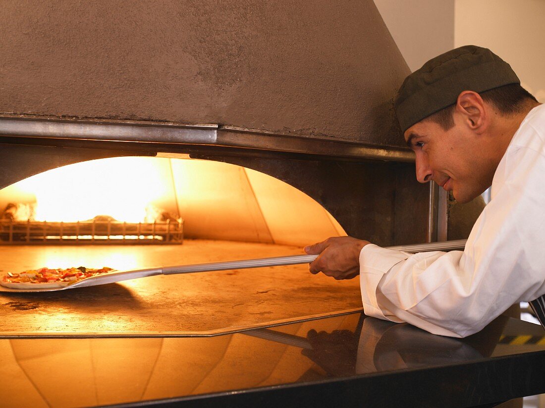 Pizzabäcker schiebt eine Pizza in den Ofen