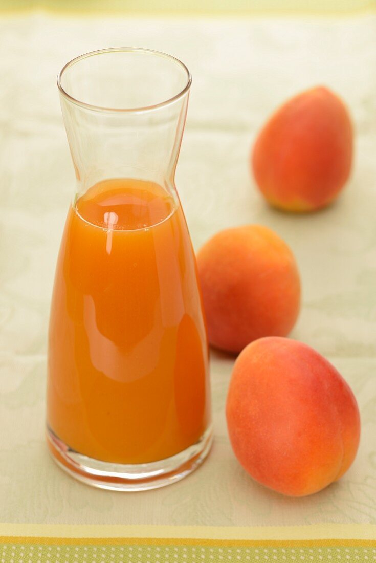 Apricot juice in a carafe with three whole apricots