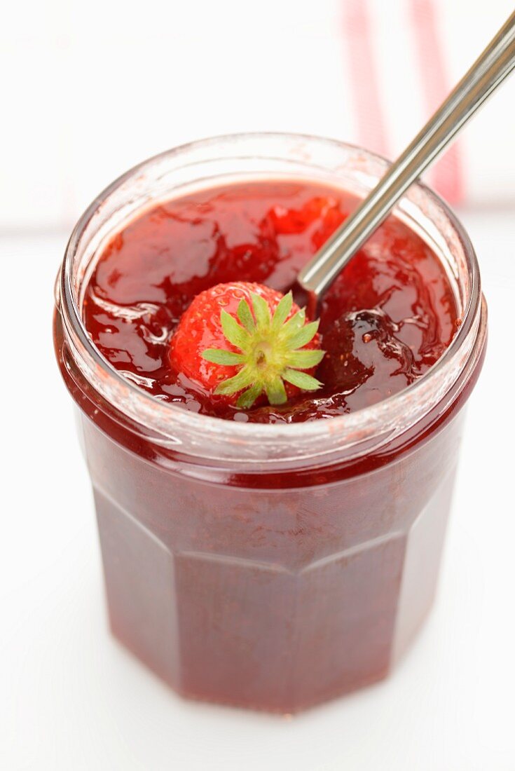 Strawberry jam in a jar with a spoon and a fresh strawberry