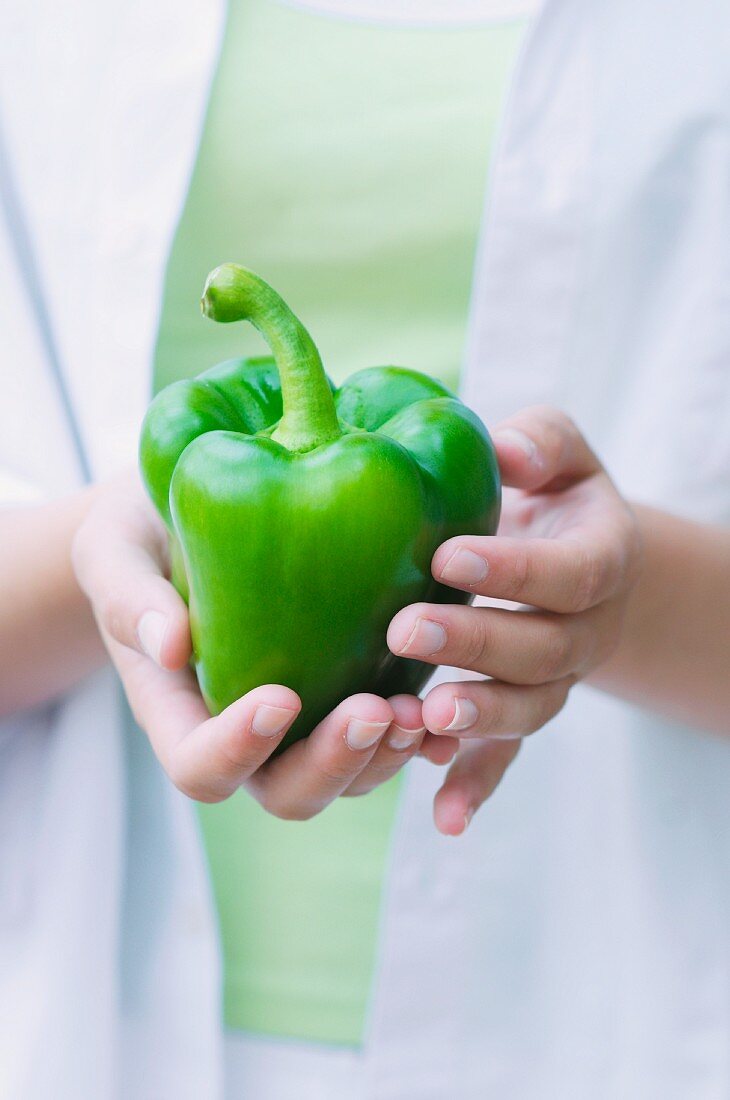A young woman holding a green pepper