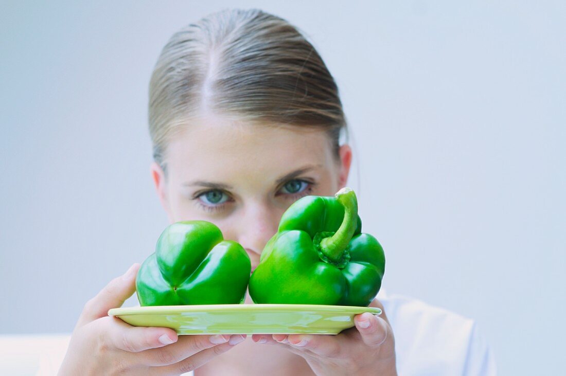 A girl holding two green peppers on a plate