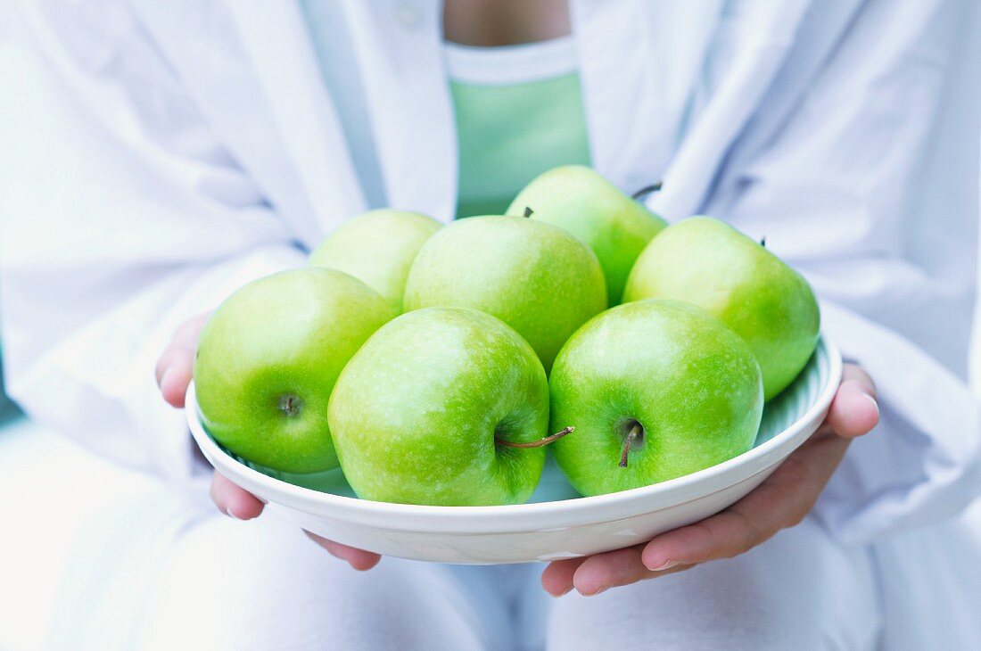 A girl holding a plate of green apples