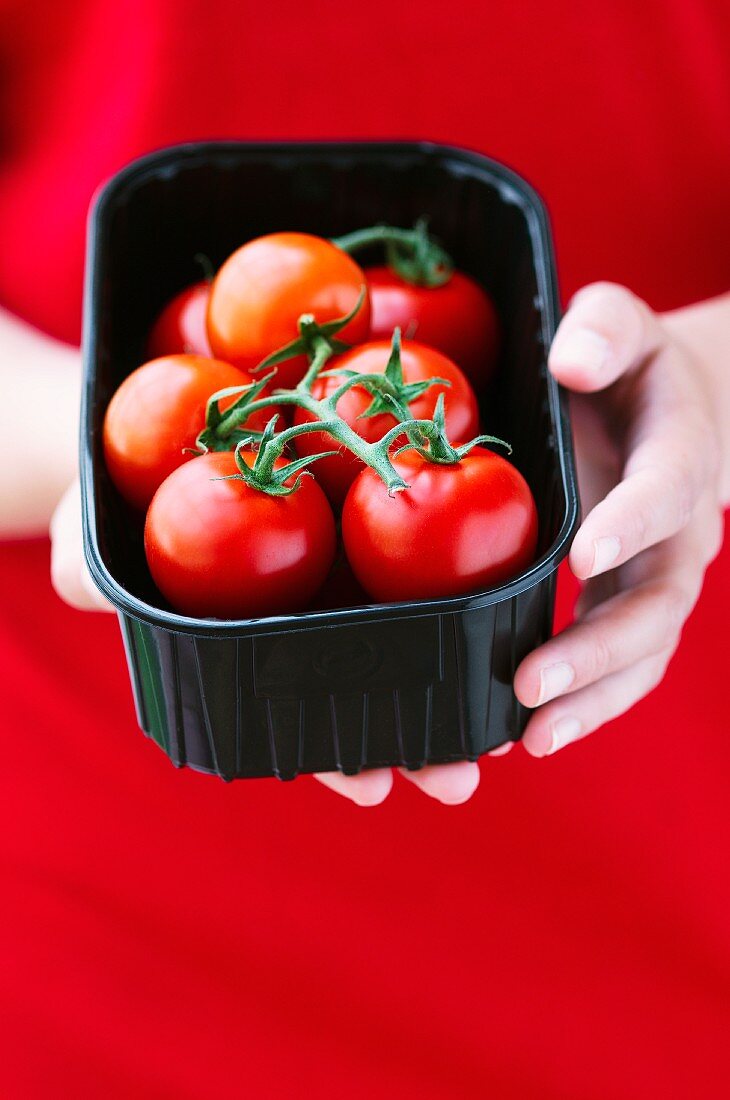 A young woman holding a plastic box of tomatoes