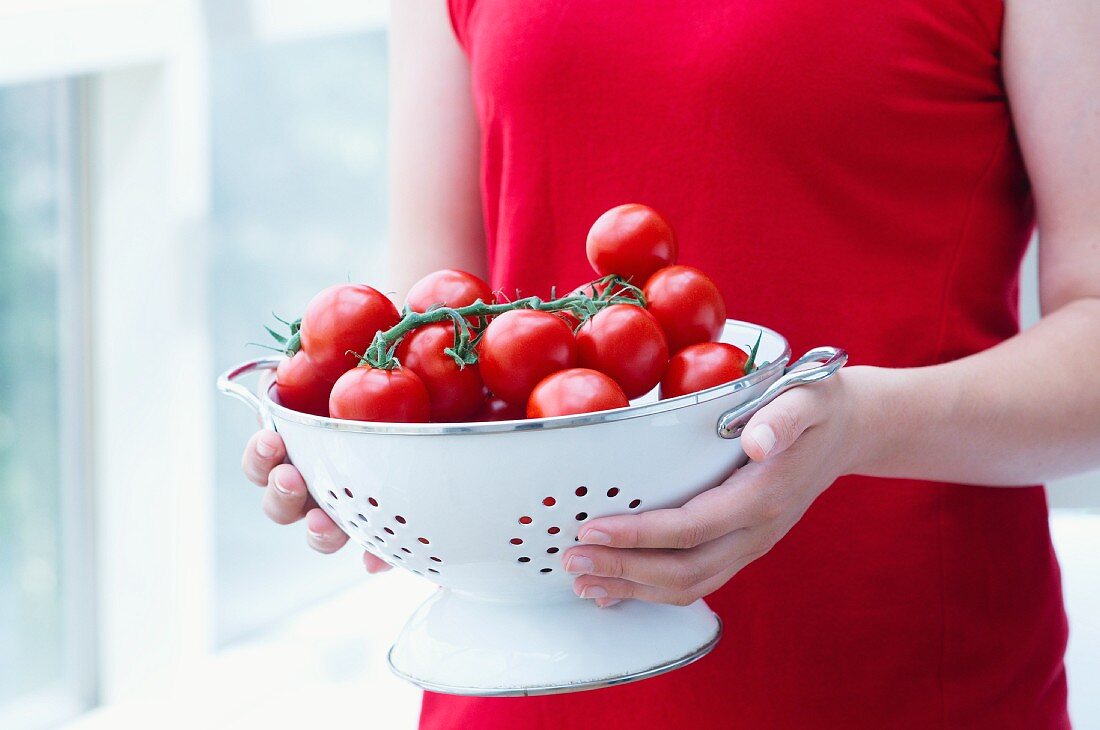A young woman holding a colander of tomatoes