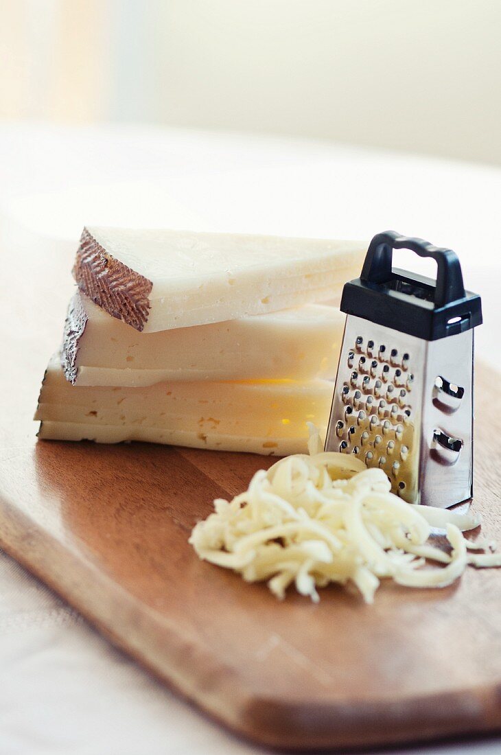 Gestapelte Käsestücke mit Käsereibe und geriebenem Käse auf einem Holzbrett