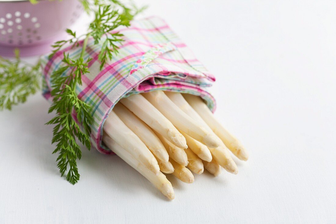 Geschälter weisser Spargel im Küchentuch mit Karottengrün