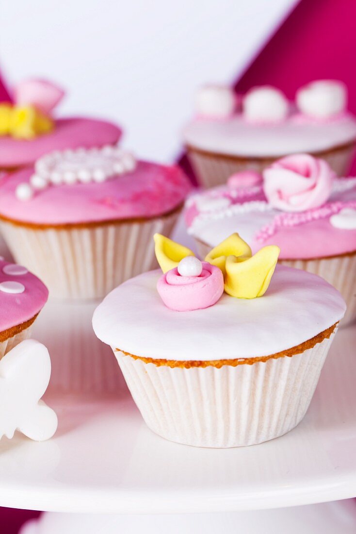 Cupcakes mit rosa und weisser Glasur und Zuckerrosen auf einer Tortenplatte