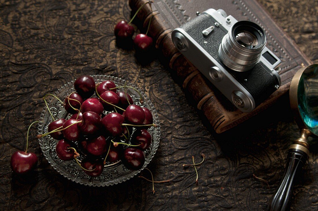 A glass bowl of sweet cherries and a camera