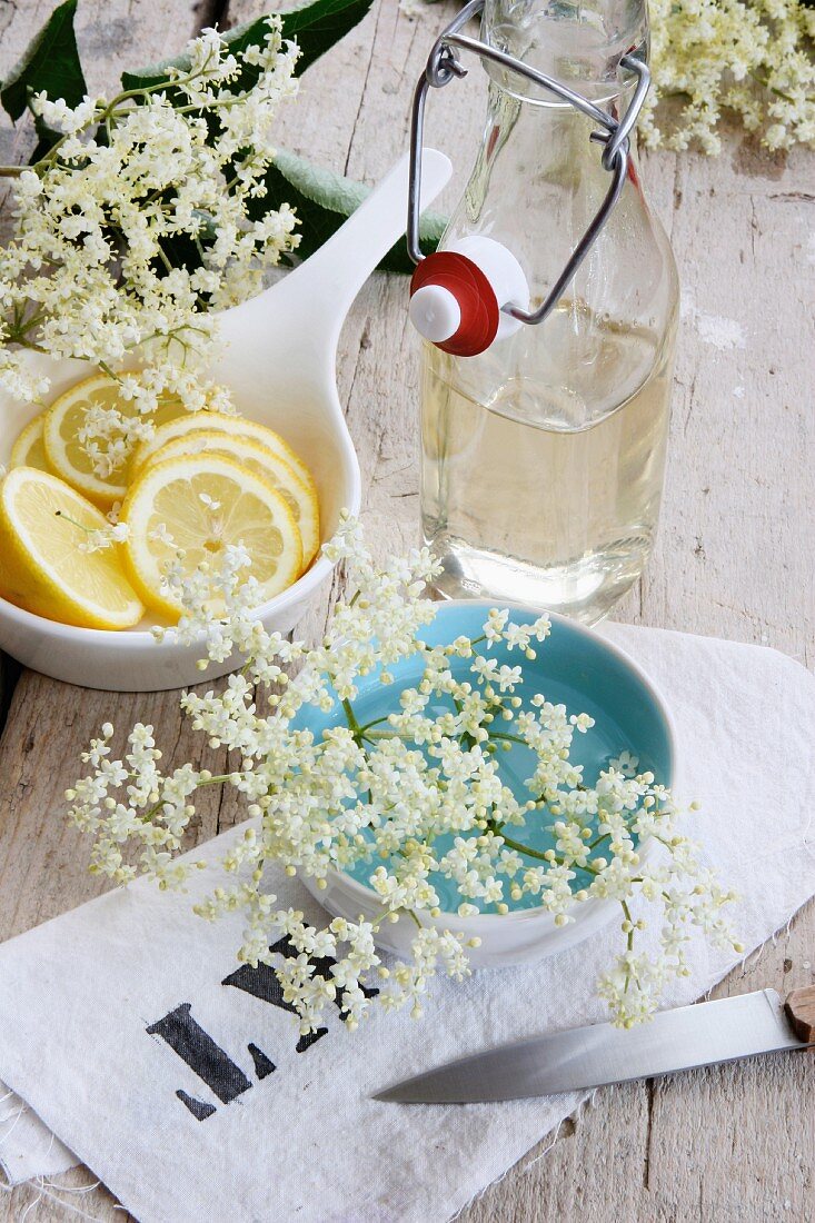 Holunderblütensaft, Zitronenscheiben und Holunderblüten auf einem bedruckten Tuch