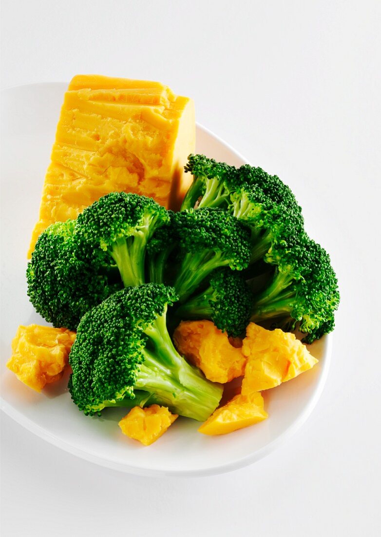 Fresh Broccoli and Chunks of Cheddar Cheese on a White Plate; White Background