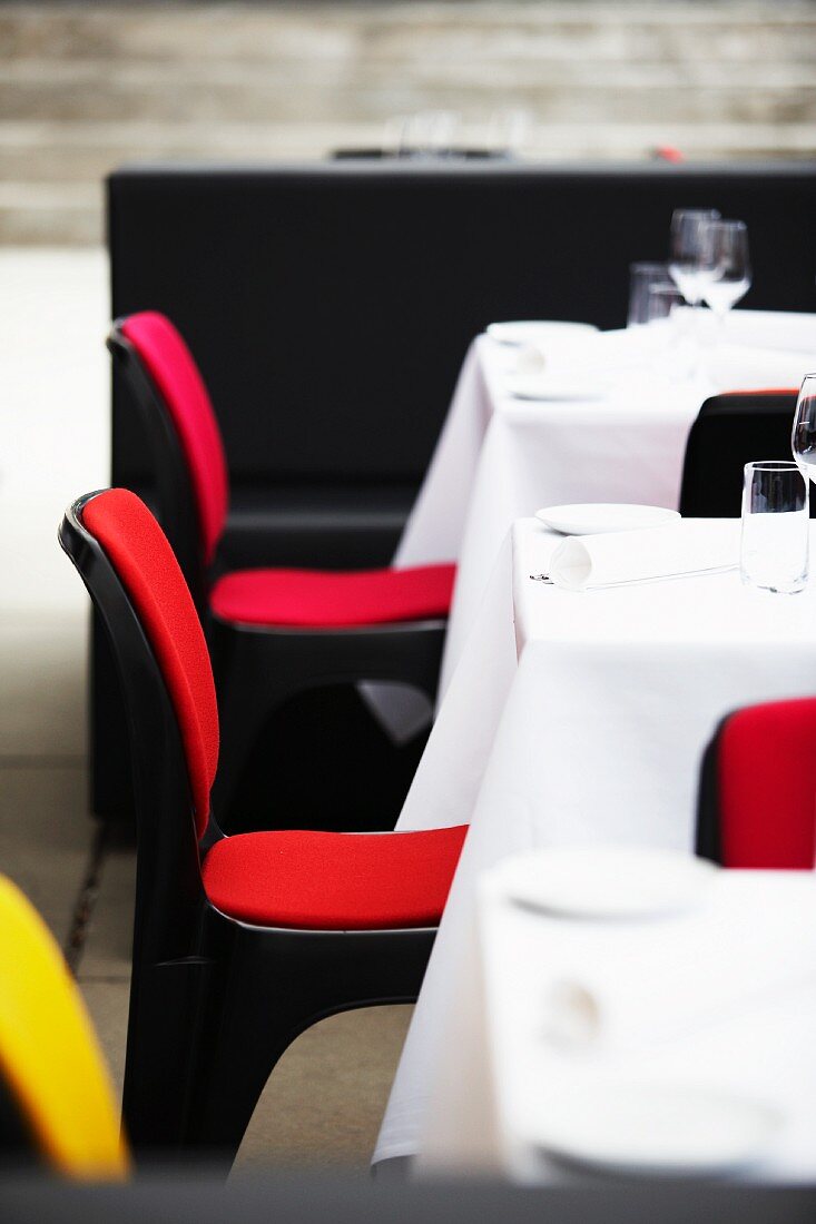 Colourful restaurant chairs in front of laid tables