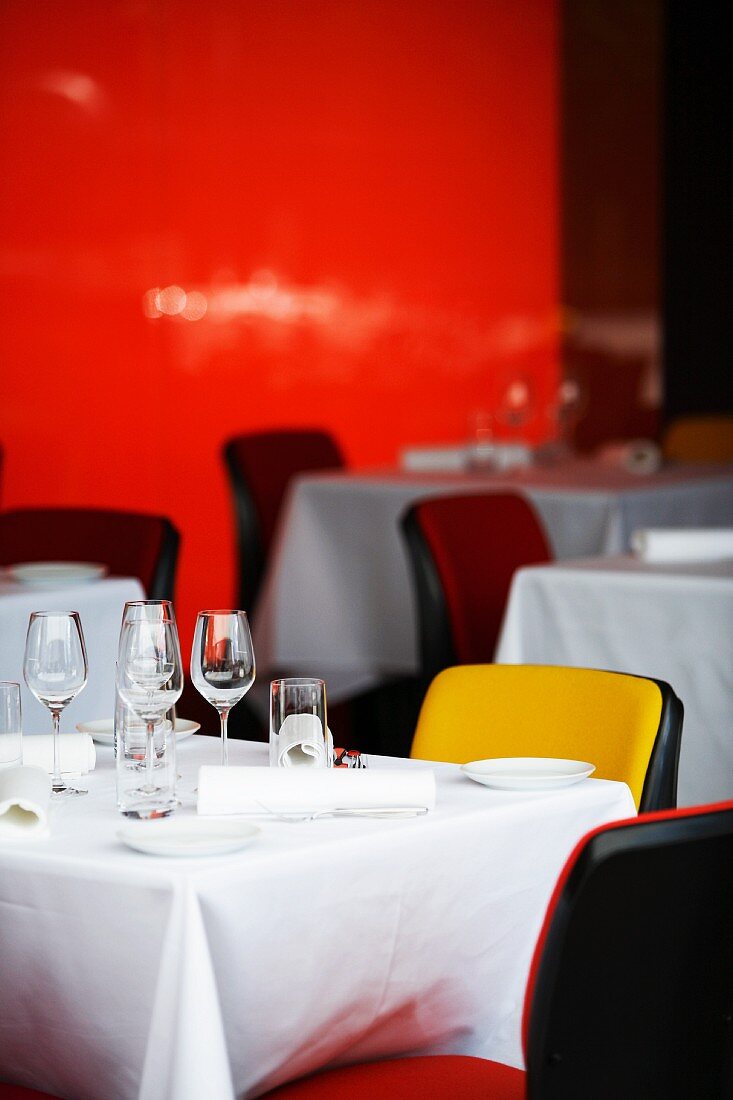Gedeckte Restauranttische mit farbenfrohen Stühlen vor einer roten Wand