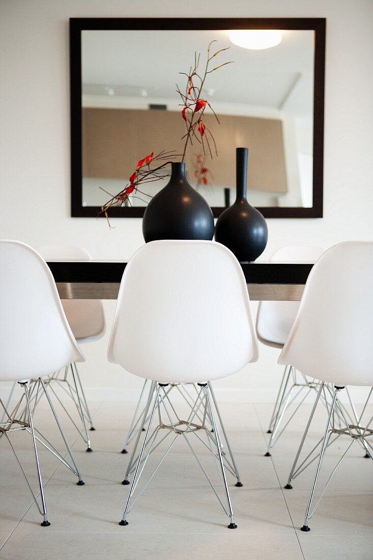 Detail of dining room with large, framed mirror on wall, black table and white designer shell chairs