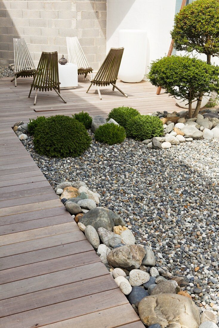 Gartenstühle auf einer gepflegten Terrasse mit getrimmten Buchsbaumbüschen in einem Kiesbett