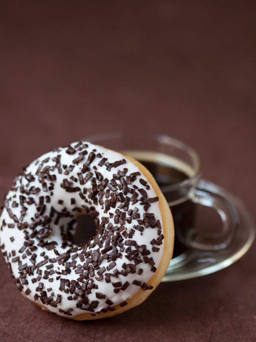 Ein Doughnut mit Zuckerglasur und Schokostreuseln und eine Tasse Kaffee