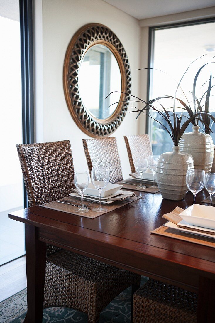 Set table and wicker chairs in dining room; round, framed mirror on wall