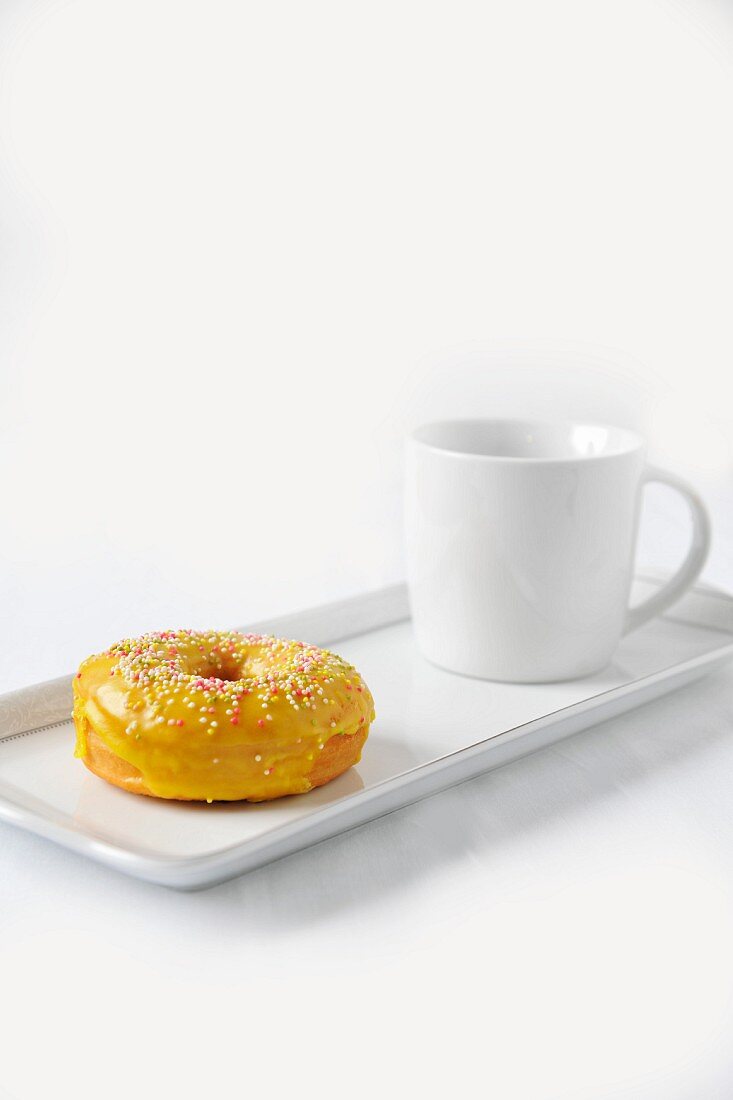 A doughnut with yellow glaze and sugar balls and a cup