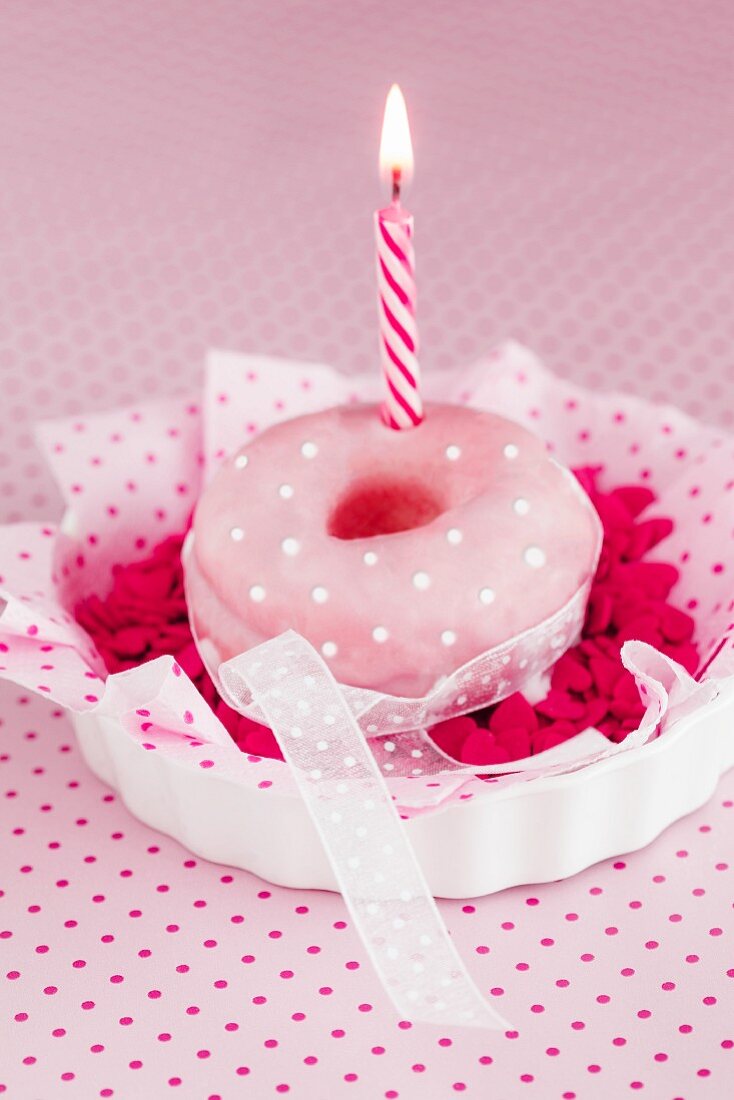A doughnut with pink glaze and a candle